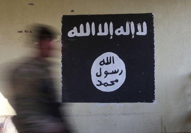 A member of the Iraqi rapid response forces walks past a wall painted with the black flag commonly used by Islamic State militants, during battle in the Wahda district of eastern Mosul, Iraq