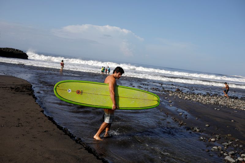 FILE PHOTO: Surfer crosses a stream at El Tunco beach in Tamanique