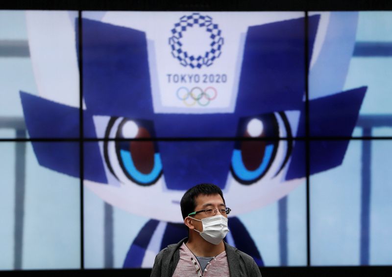 A man wearing a protective face mask stands in front of a screen showing Tokyo 2020 Olympic Games mascot Miraitowa amid the coronavirus disease (COVID-19) outbreak, in Tokyo