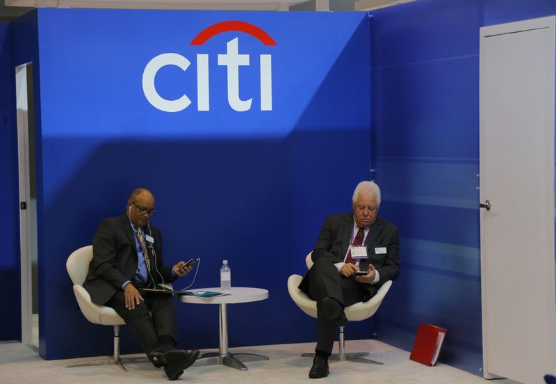 Two men look at their mobile phones under the Citigroup logo at the SIBOS banking and financial conference in Toronto