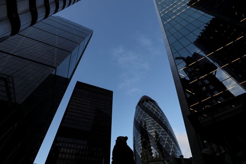 A pedestrian walks past skyscrapers in the financial district in London