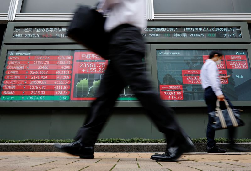 Passersby wearing protective masks walk past an electronic board showing Japan's Nikkei average, in Tokyo