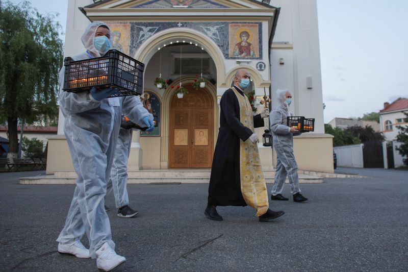 Orthodox priest Bogdan Teleanu, wearing a face mask, and volunteers carrying crates of lit candles while dressed in protective suits, head to the surrounding streets to bring holy light to people celebrating Orthodox Easter