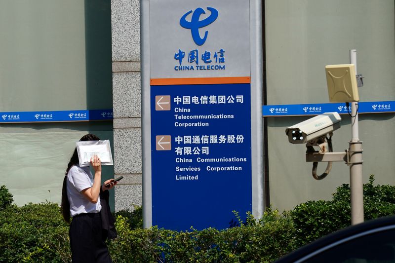 FILE PHOTO: FILE PHOTO: Woman shields herself from the sun as she walks past an office building of China Telecom, in Beijing