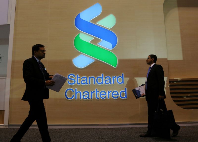 FILE PHOTO: People pass by the logo of Standard Chartered plc at the SIBOS banking and financial conference in Toronto