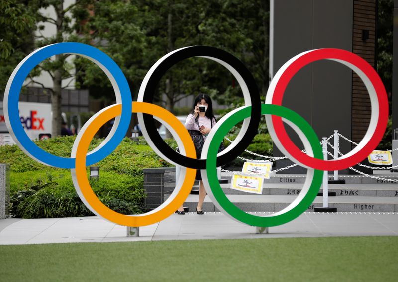 A woman wearing a protective mask amid the coronavirus disease (COVID-19) outbreak, takes a picture of the Olympic rings in front of the National Stadium in Tokyo