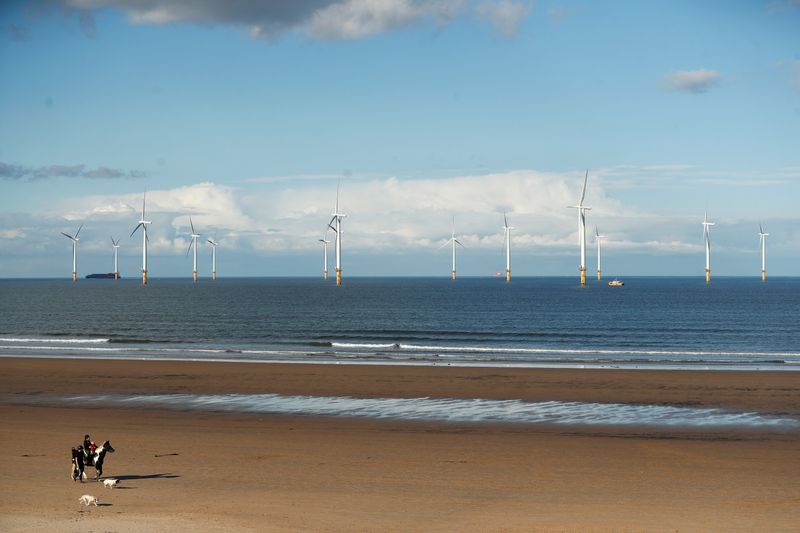 Wind turbines are seen in the background as people stroll along Redcar Beach in Redcar