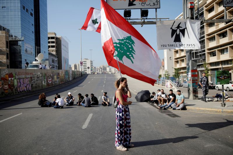 FILE PHOTO: A woman holds a Lebanese flag as she stands at a roadblock during ongoing anti-government protests in Beirut