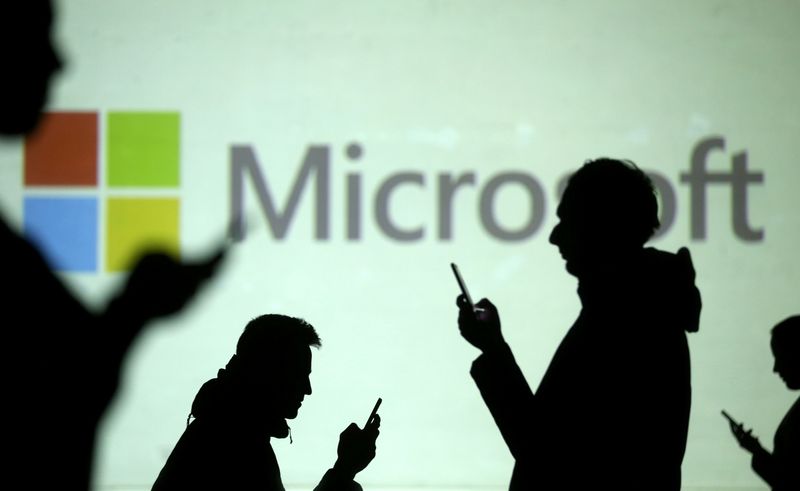 FILE PHOTO: Silhouettes of mobile users are seen next to a screen projection of Microsoft logo in this picture illustration