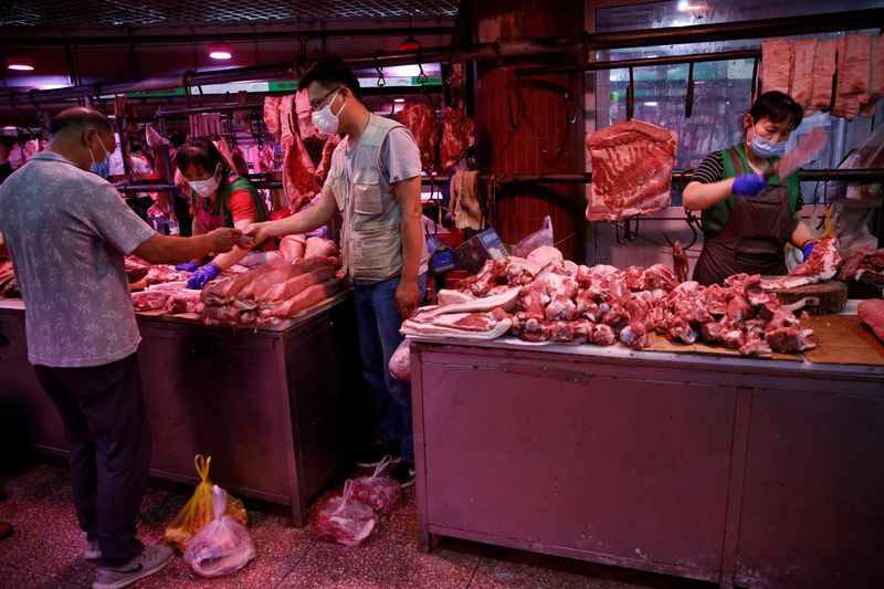 customer wearing a face mask pays for pork as a vendor chops pork meat inside the Yuegezhuang wholesale market, following new cases of coronavirus disease (COVID-19) infections in Beijing