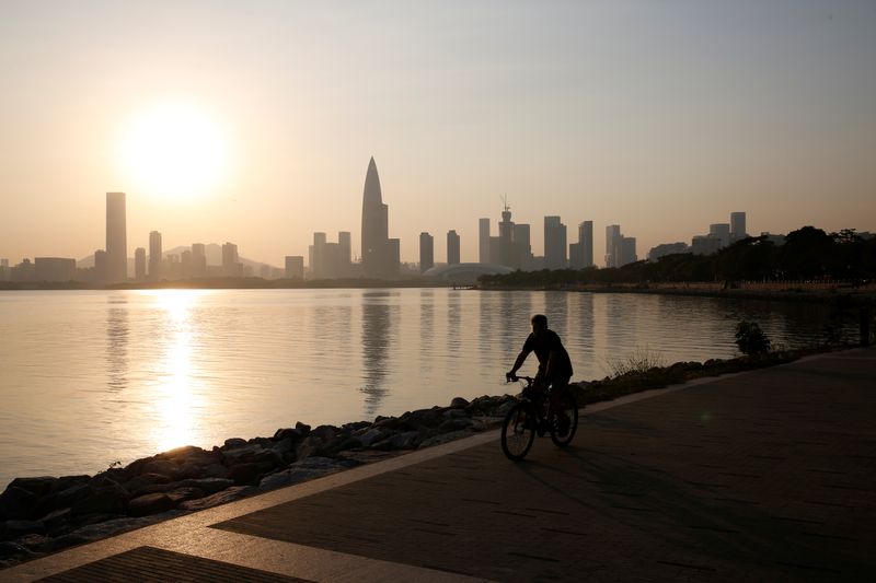 A person rides a bicycle during sunset in front of Shenzhen's highrise buildings in Shenzhen.