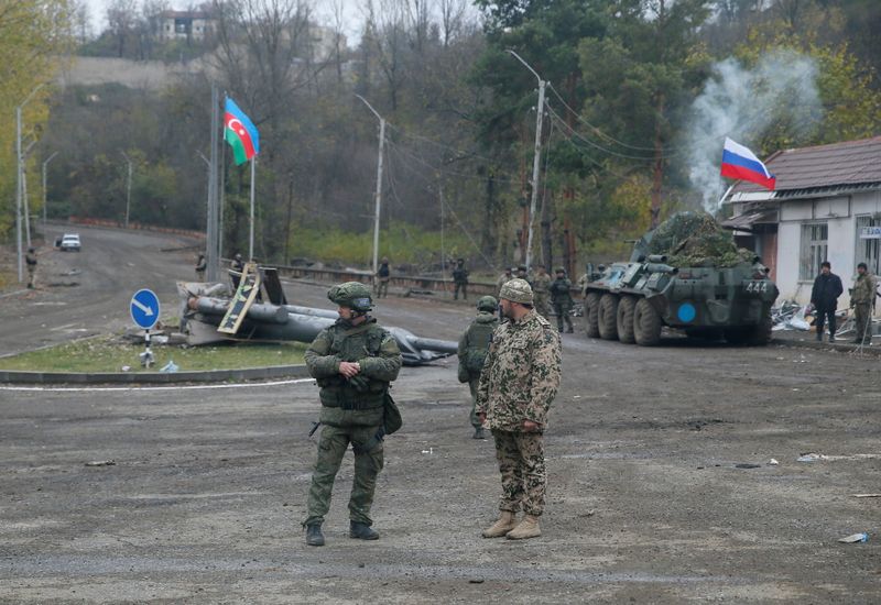 An Azerbaijani service member and a Russian peacekeeper stand guard at a checkpoint on the outskirts of Shusha