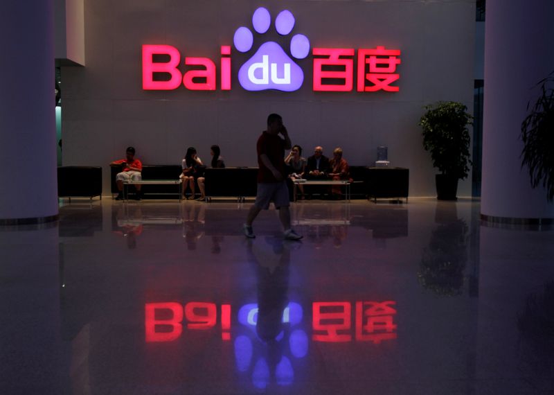 A employee uses his mobile phone as he walks past the company logo of Baidu at its headquarters in Beijing