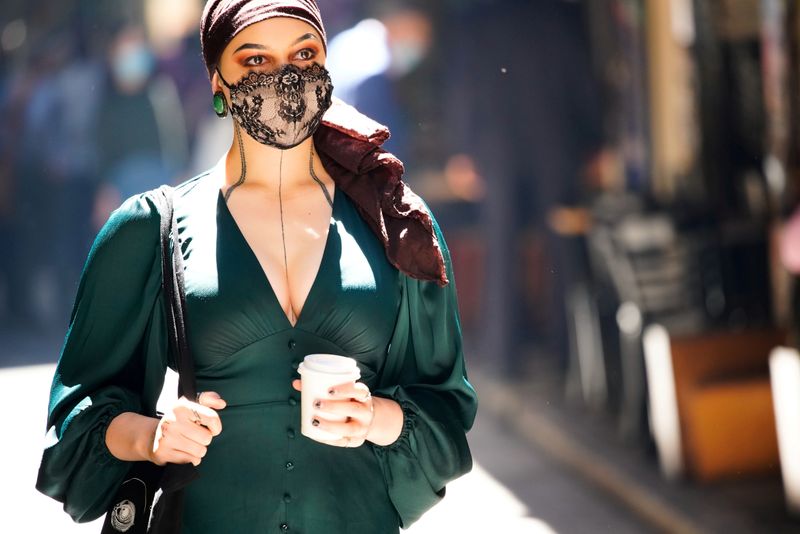 FILE PHOTO: A woman wearing a face masks walks past cafes after coronavirus disease restrictions were eased in Melbourne