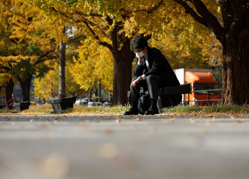 A man wearing a protective face mask pauses under colourful autumn leaves, amid the coronavirus disease (COVID-19) outbreak, in Tokyo