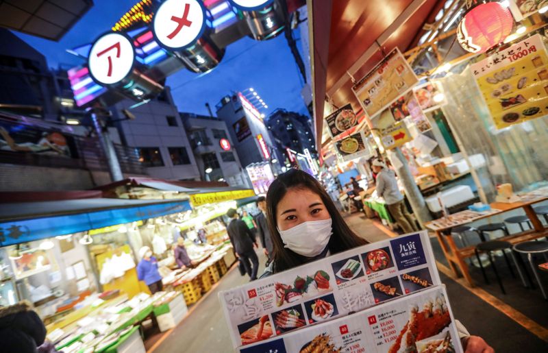 FILE PHOTO: A woman wooing visitors for her restaurant wears a protective face mask in Tokyo