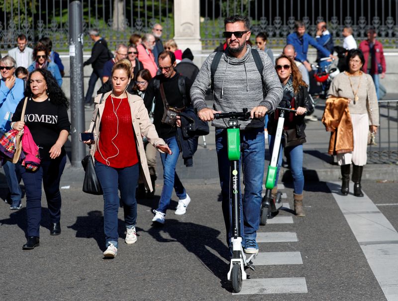 FILE PHOTO: People ride dock-free electric scooters Lime-S by California-based bicycle and scooter sharing service Lime, through a crosswalk in Madrid