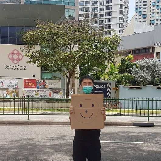 Jolovan Wham wears a mask and holds a cardboard with a drawing of a smiley face in Singapore