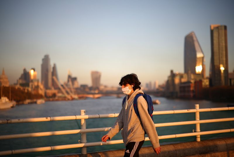 A man wearing a protective face mask walks over Waterloo Bridge during sunset, amid the coronavirus disease (COVID-19) outbreak, in London