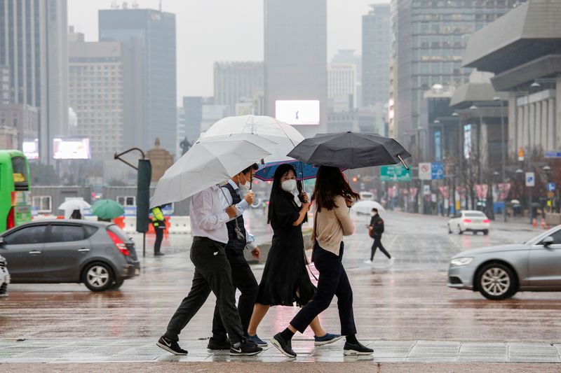 Pedestrians wearing masks walk with umbrellas as it rains amid the coronavirus disease (COVID-19) pandemic in central Seoul