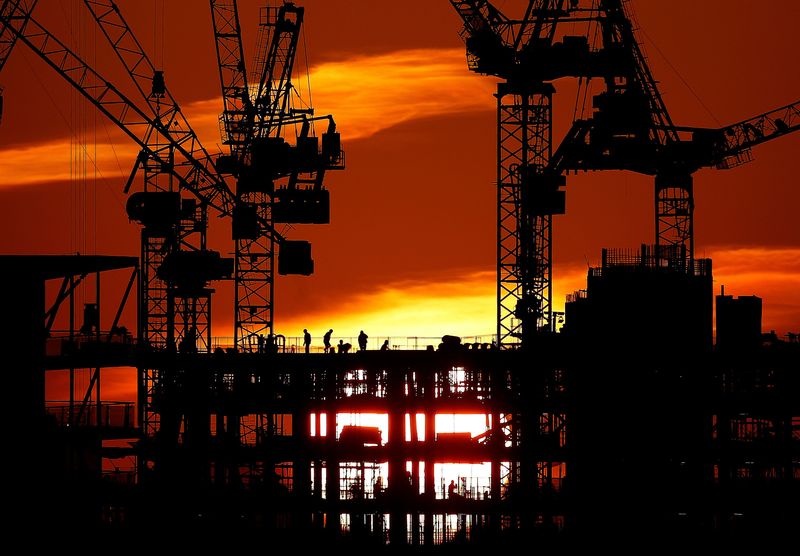 Workers are seen as the sun sets behind a construction site in London