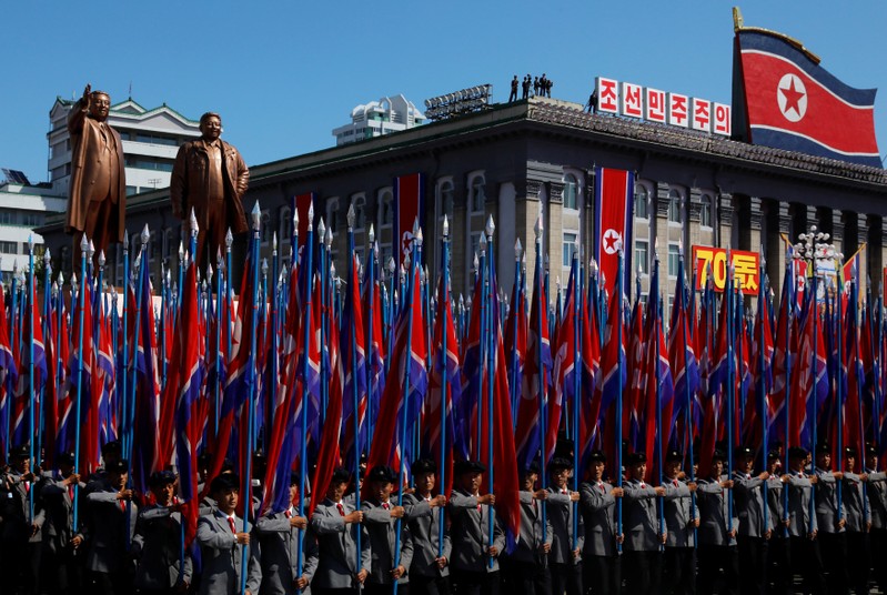 People carry flags in front of statues of North Korea founder Kim Il Sung (L) and late leader Kim Jong Il during a military parade marking the 70th anniversary of North Korea's foundation in Pyongyang