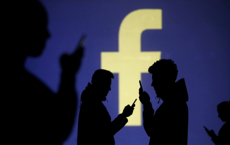 FILE PHOTO: Silhouettes of mobile users are seen next to a screen projection of Facebook logo in this picture illustration