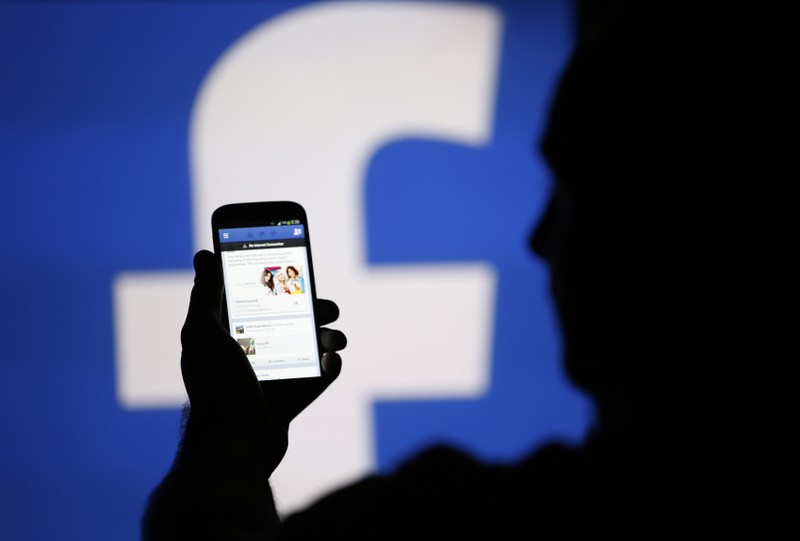 A man is silhouetted against a video screen with an Facebook logo as he poses with an Samsung S4 smartphone in this photo illustration taken in the central Bosnian town of Zenica