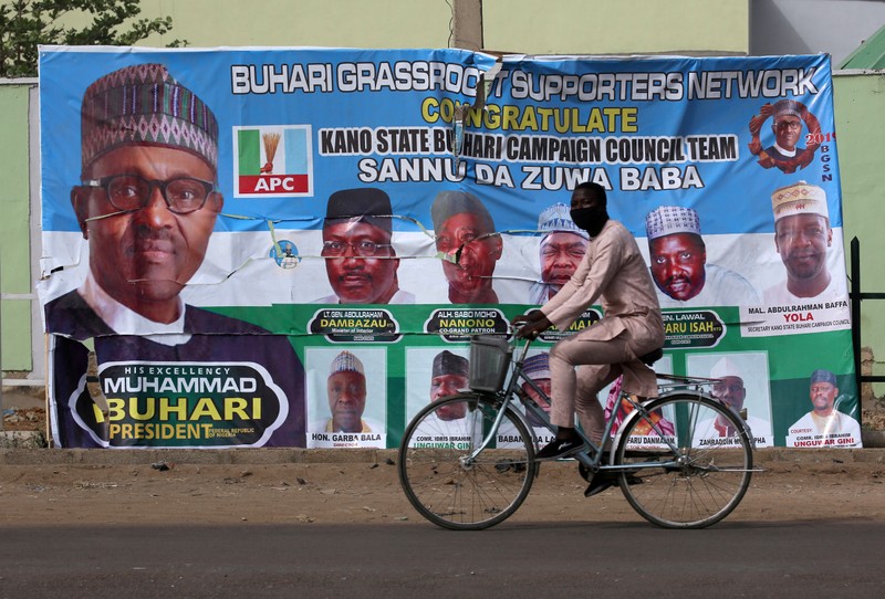 FILE PHOTO: A cyclist drives pasts a campaign poster for President Muhammadu Buhari in a street after the postponement of the presidential election in Kano