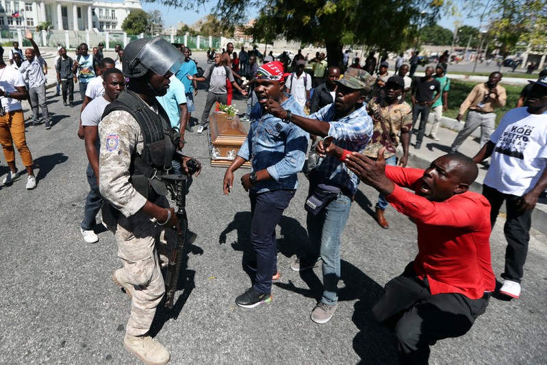 Local residents argue with a policeman while the casket of a man shot dead during anti-government protests lies on the ground in Port-au-Prince