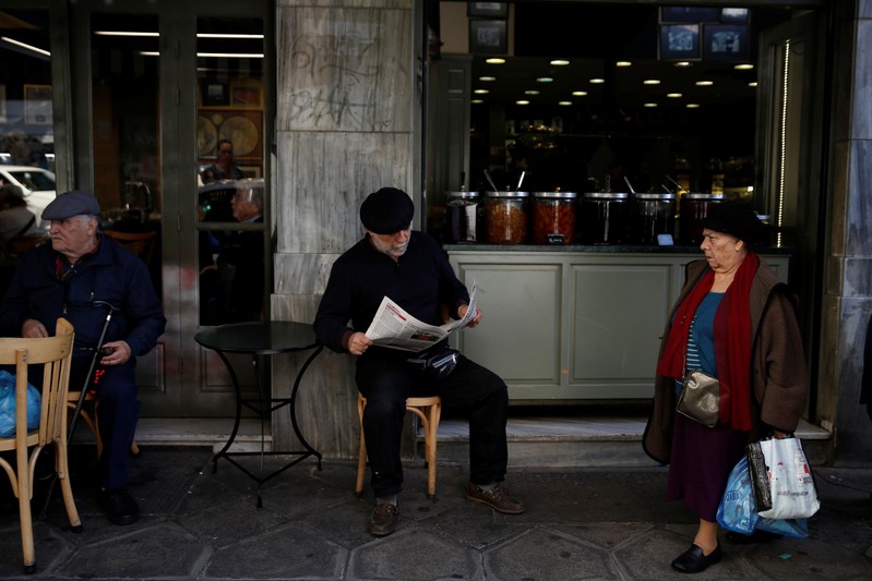 A man reads a newspaper at a coffee shop in central Athens