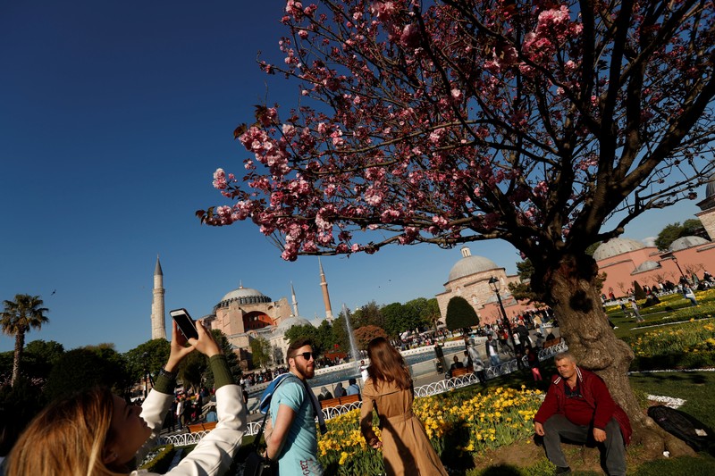A foreign tourist, with the Byzantine-era monument of Hagia Sophia in the background, take pictures at Sultanahmet square in Istanbul