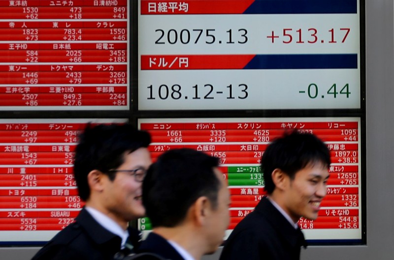 FILE PHOTO: Pedestrians walk past electronic board showing the Nikkei stock index outside a brokerage in Tokyo