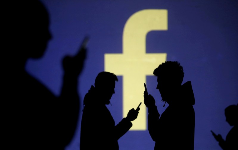 FILE PHOTO: Silhouettes of mobile users are seen next to a screen projection of Facebook logo in this picture illustration