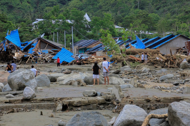 eople stand as they look at damaged houses after a flash flood in Sentani, Papua