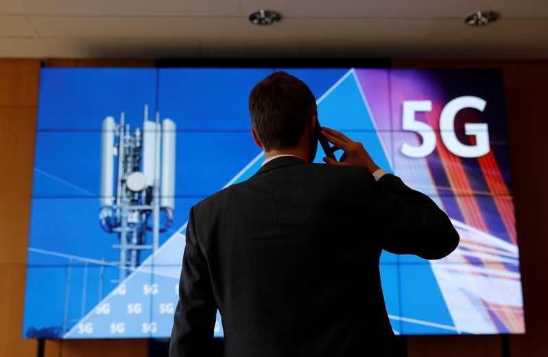 An employee of Germany's Federal Network Agency (Bundesnetzagentur) uses his mobile phone in front of a screen set up for the auction of spectrum for 5G services at the Bundesnetzagentur headquarters in Mainz