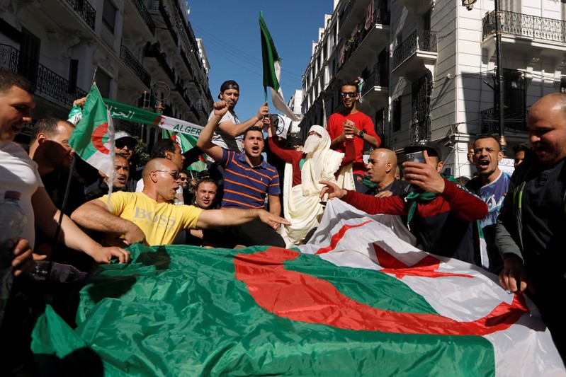 People carry their national flags as they protest over President Abdelaziz Bouteflika's decision to postpone elections and extend his fourth term in office, in Algiers