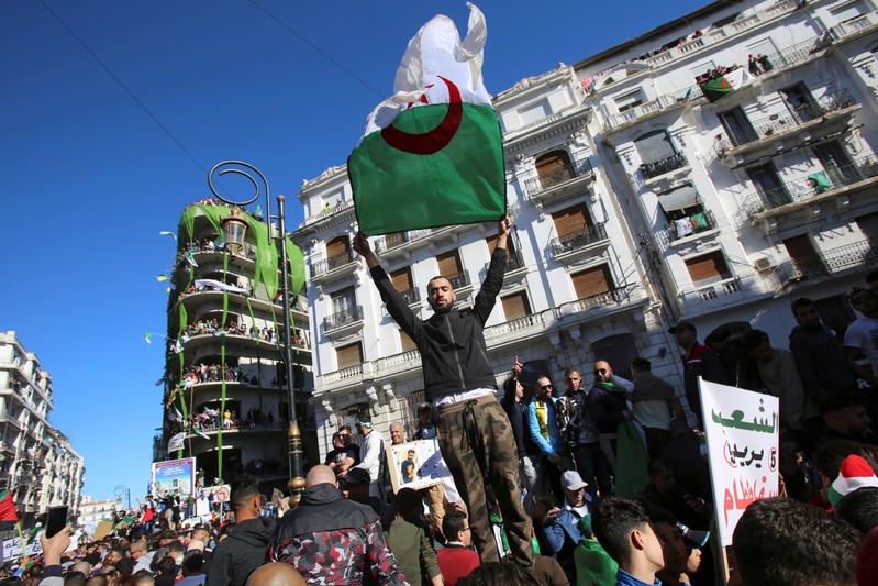 FILE PHOTO: Demonstrator carries a national flag during protest over President Abdelaziz Bouteflika's decision to postpone elections and extend his fourth term in office, in Algiers