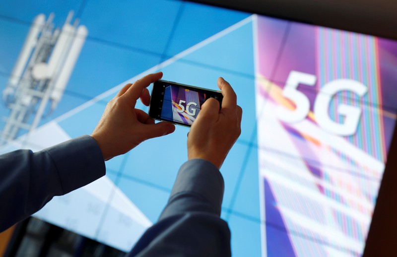 A journalist uses his mobile phone to take a picture of the 5G logo prior to the auction of spectrum for 5G services at the Bundesnetzagentur head quarters in Mainz