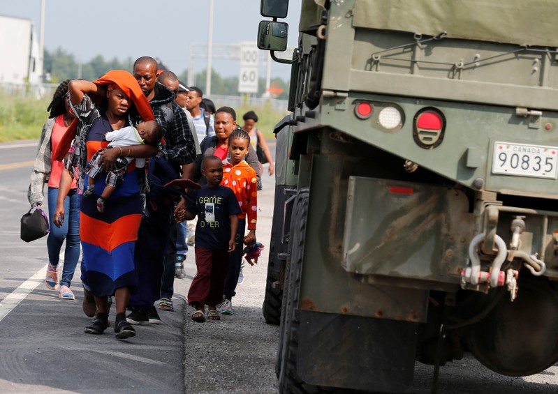 FILE PHOTO: A group of asylum seekers pass a Canadian army vehicle as they walk down the street while escorted from their tent encampment to be processed at Canada Border Services in Lacolle