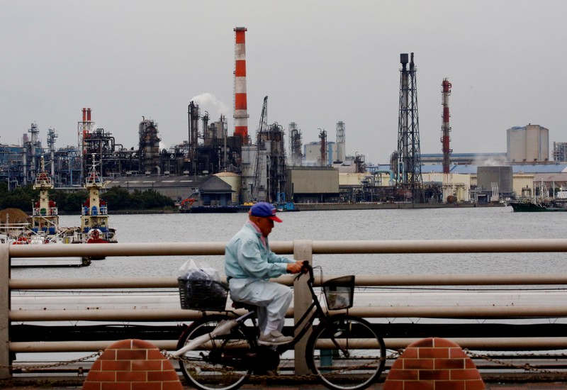 FILE PHOTO: A man cycles past chimneys of facotries at the Keihin Industrial Zone in Kawasaki