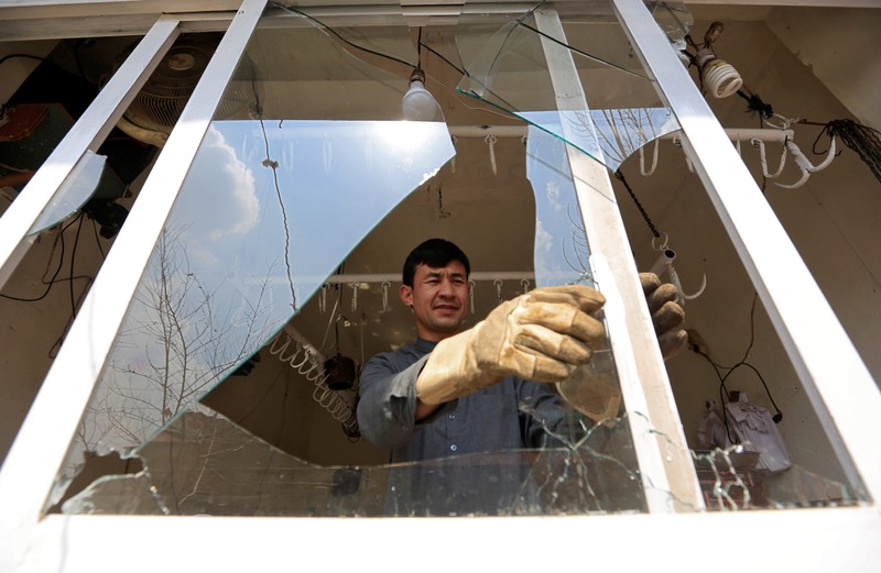 A man removes broken glass from a window after multiple explosions in Kabul