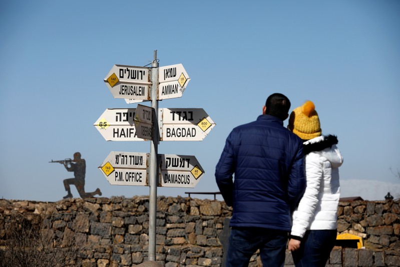 FILE PHOTO: A couple look towards signs pointing out distances to different cities,at an observation post in the Israeli-occupied Golan Heights