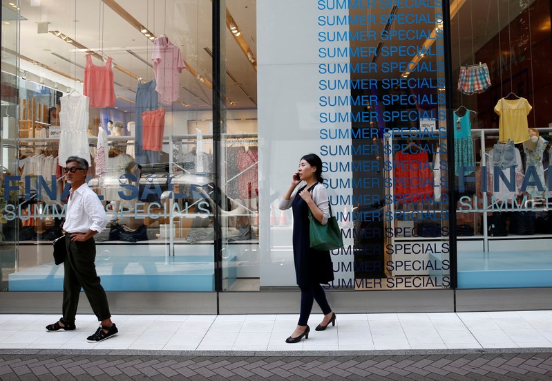 FILE PHOTO: Pedestrians stand in front of sale signs on a shopfront at a shopping district in Tokyo