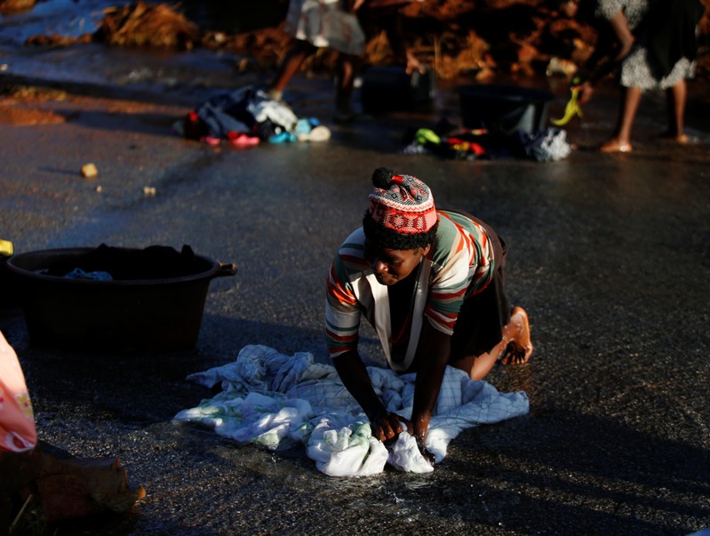 A woman washes clothes in a river of water running across a road that was created after Cyclone Idai in Chimanimani