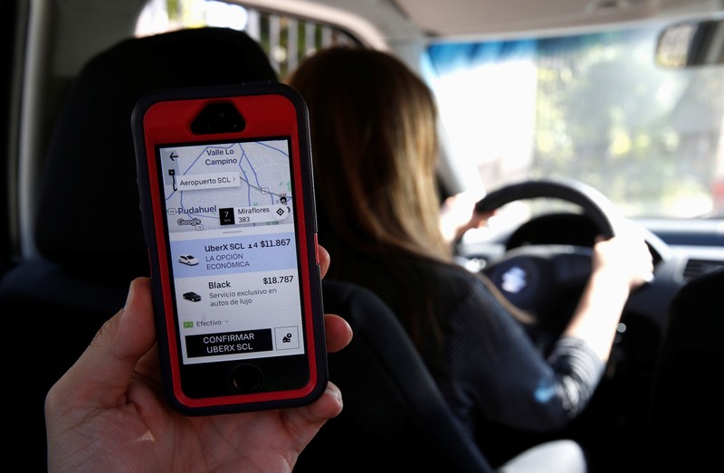 A cell phone with the Uber transport technology app, with the destination and its cost to the international airport, is seen inside a car with an Uber driver, in Santiago