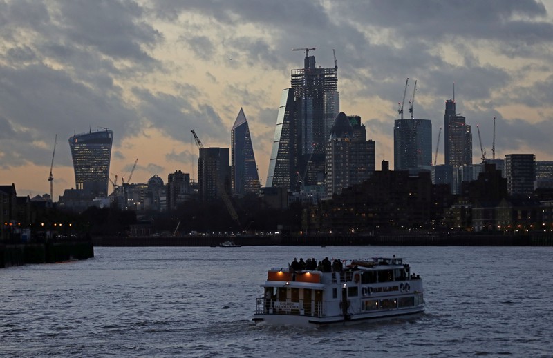 FILE PHOTO: A river boat cruises down the River Thames as the sun sets behind the Canary Wharf financial district of London
