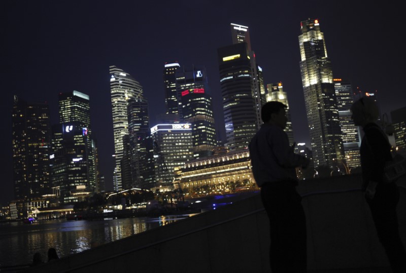 People chat as the skyline of Singapore's financial district is seen in the background