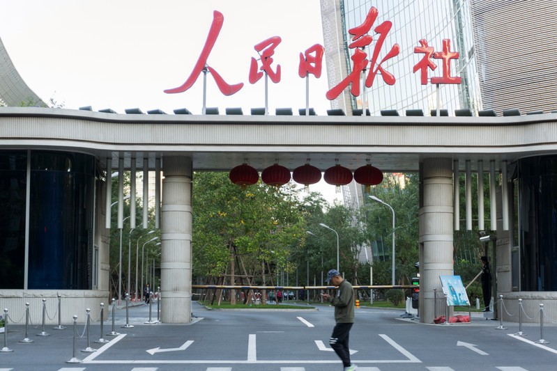 Man holding a smartphone walks past the headquarters of Chinese state newspaper People's Daily in Beijing