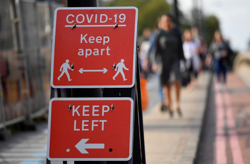 FILE PHOTO: Pedestrians walk near public health signs, whilst the reproduction